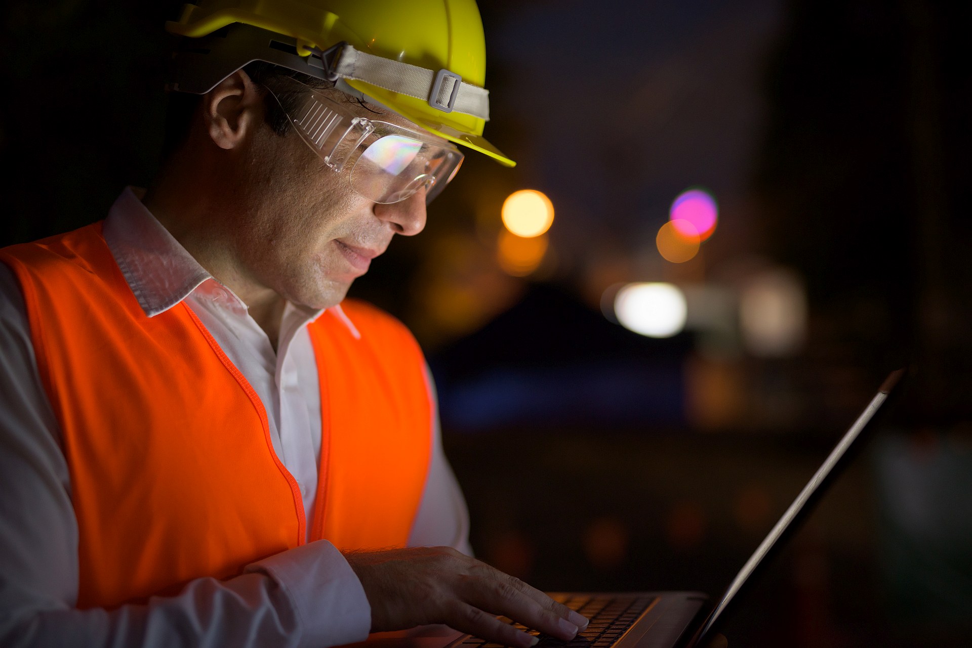 Site engineer in hard hat and hi-vis working on a laptop at night