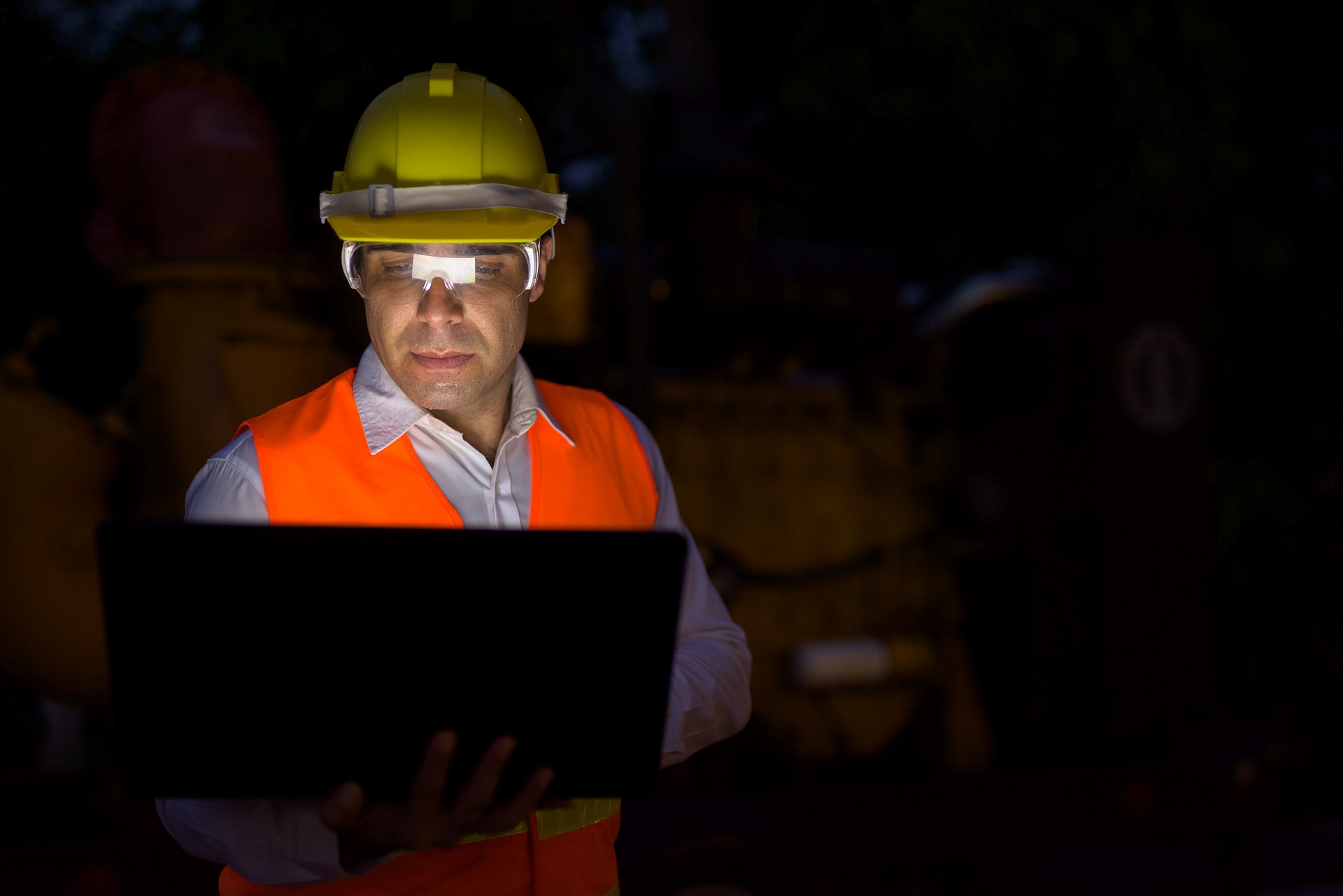 Construction engineer in hard hat and safety glasses using a laptop on site